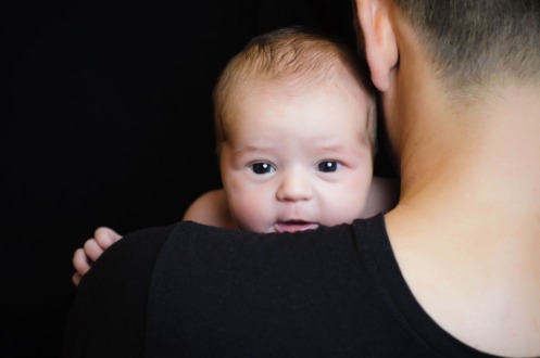 Ein Baby blickt über die Schulter eines Mannes, welcher dieses hält.