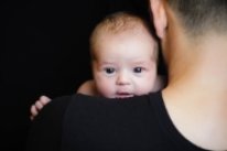 ein Baby blickt über die Schulter eines vom Bild abgewandten Mannes